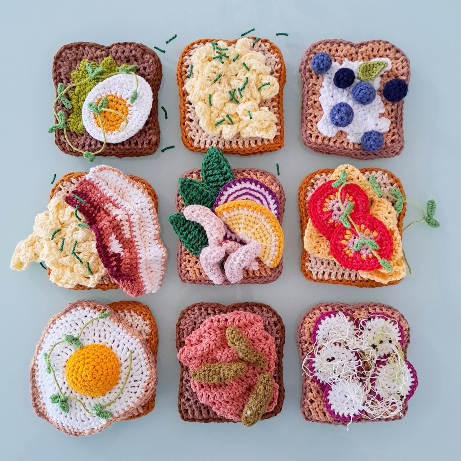 Crocheted Food - a variety of 9 crocheted sandwiches in rows of 3. From let to right, boiled egg slice, scrambled egg, berries and cream cheese, bacon and eggs, and I'm not entirely sure about the rest except the bottom left has a sunny side up egg.